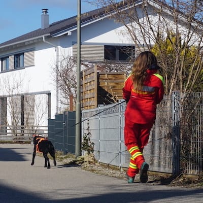 Schwarzer Hund mit langer Leine und Person mit rot gelben Einsatzklamotten.